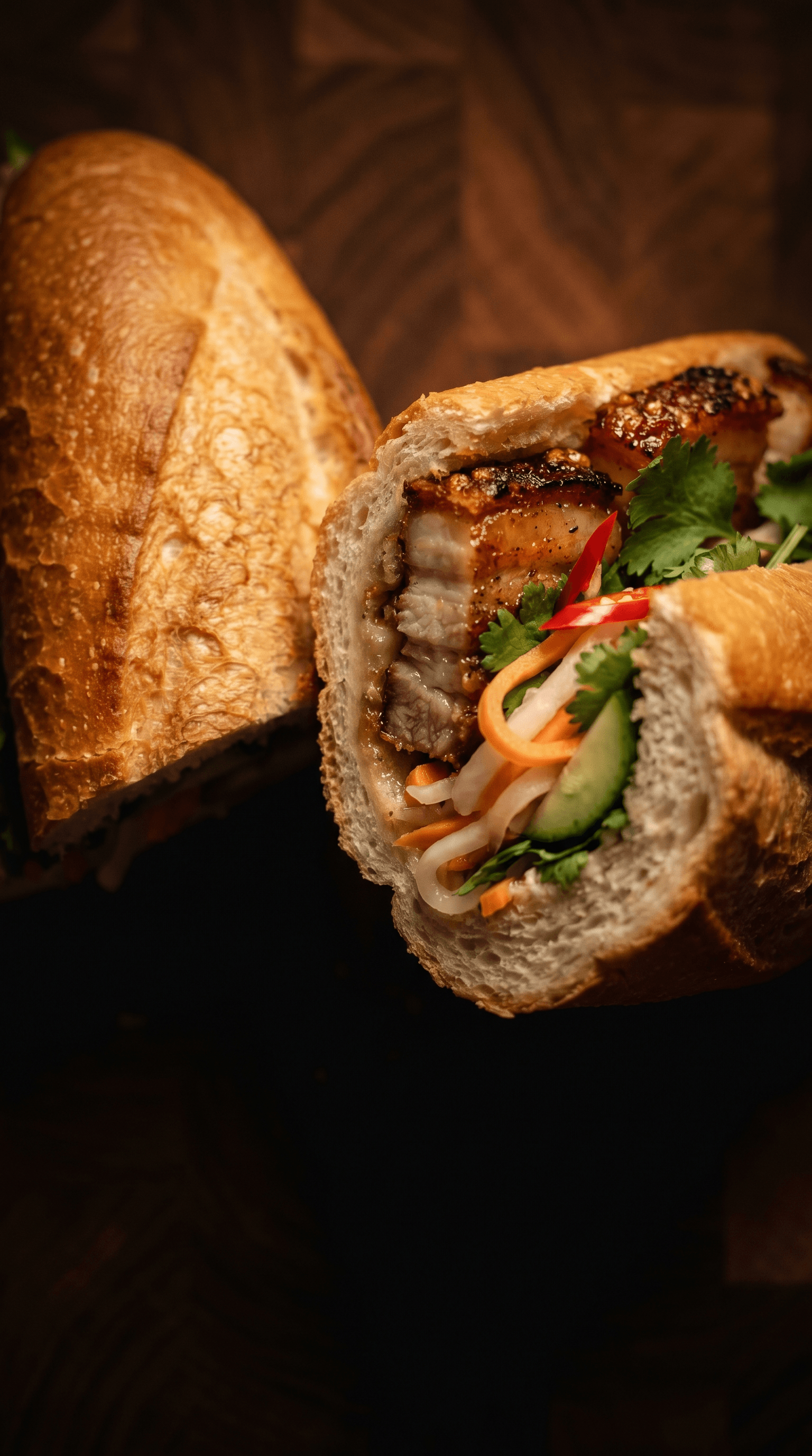 Crispy pork belly bánh mì, cross-section showing layered baguette, pork belly, pickled vegetables and herbs